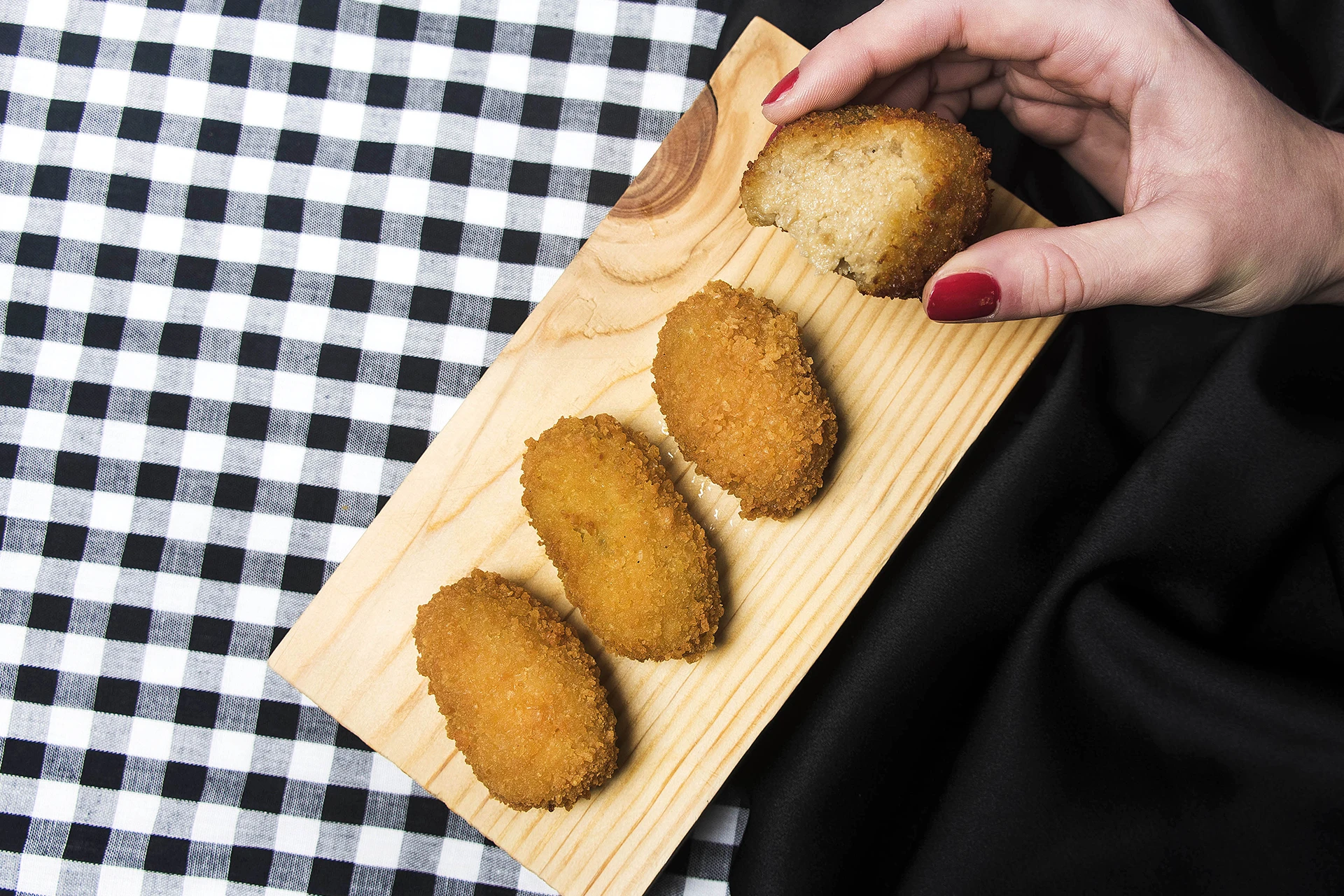 Imagen de varias croquetas de Motril sobre una tabla de madera y una de ellas sostenida con la mano de una mujer