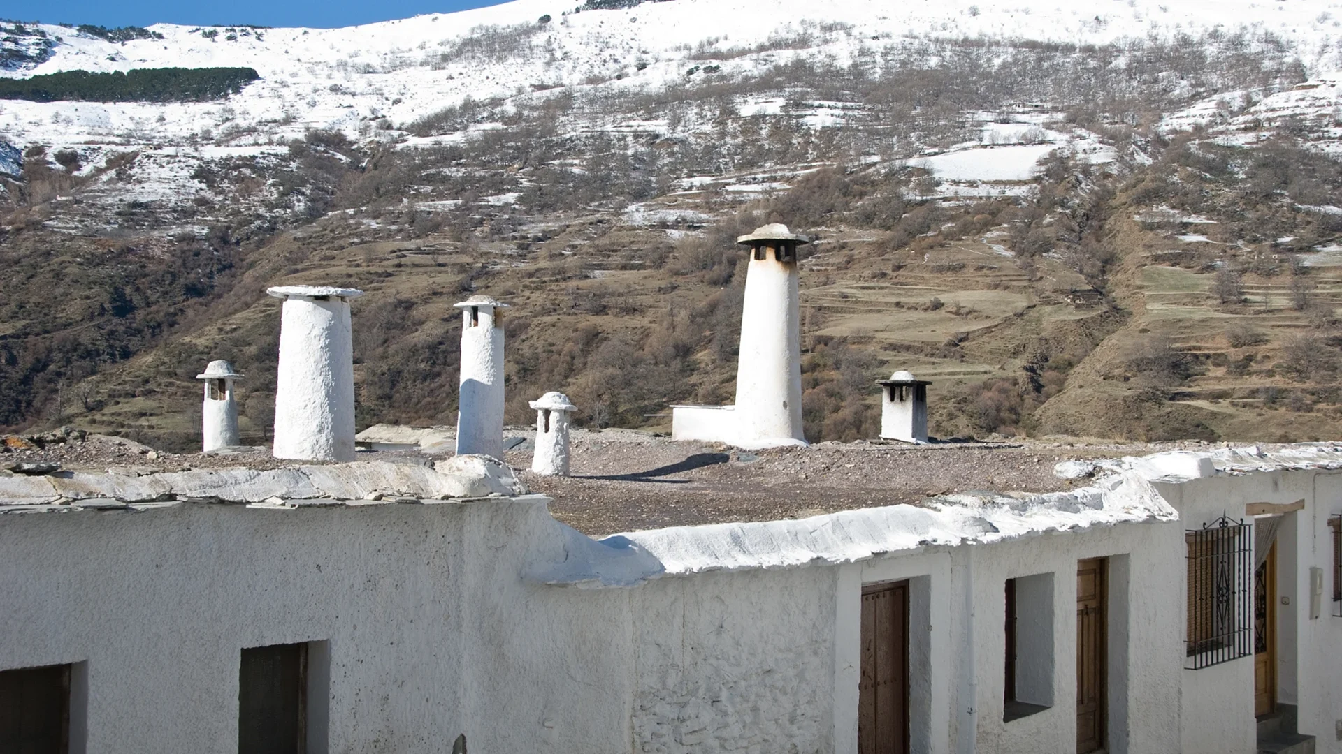 Imagen de unas casas de un típico pueblo de La Alpujarra de Granada con Sierra Nevada de fondo